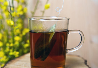 close-up of glass with hot tea and teabag and yellow flowers