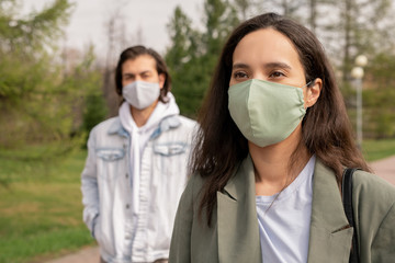 Pretty young brunette woman in protective mask walking in public park