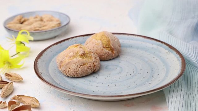 male hand puts almond cookies from a ceramic plate on a white background and blue textile. Side view, close up.