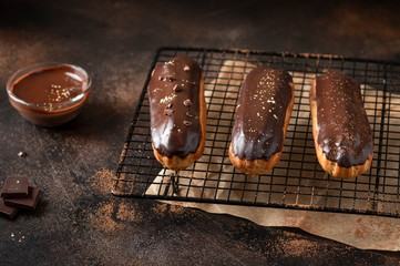 3 eclairs (profitrolls) decorated with different sprinkles on a brown concrete background....