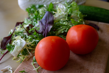 fresh vegetables on the table, red and pink two tomatoes, cucumber, Peking cabbage and lettuce leaves are lying on the cutting Board