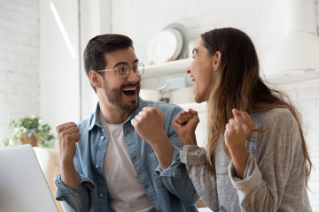 Excited millennial couple feel euphoric winning online lottery on laptop at home, overjoyed young...