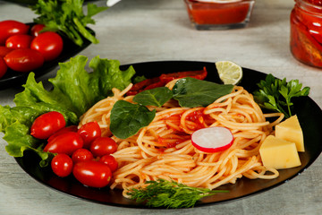 Spaghetti with tomato sauce, cherry tomatoes and basil on a dark background. Tasty appetizing classic italian spaghetti pasta with tomato sauce, cheese parmesan and basil on plate on dark table. 