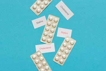 Lowering blood cholesterol with statin tablets, blister packs with pills on a blue background