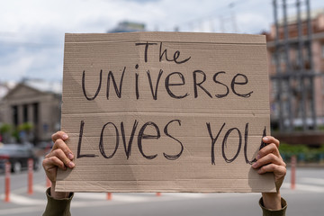 Positive thinking supportive message from the Universe loves you.  Hands holding banner outside on...