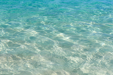 Fototapeta na wymiar Very clear water plays with sun glare on small waves. Ocean in clear calm weather.Abstract. Background.