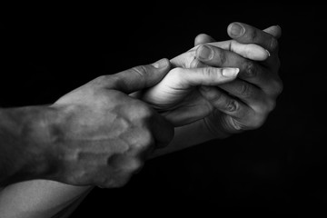 a man holds a woman's hand in his own against a dark background. close up. black and white photo