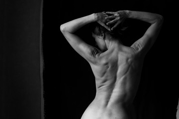 a beautiful naked woman is standing with her back raised her hands behind her head
