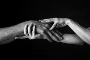 a woman gently holds a man's hand in her own against a dark background. close up. black and white photo