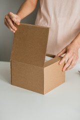 Woman opens a cardboard box, the parcel on a white table. Delivery concept