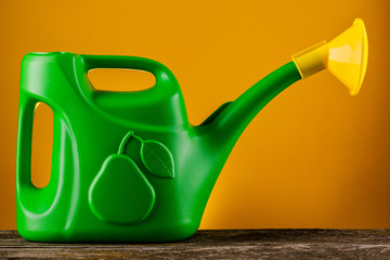 Green plastic watering can on a wooden table on a yellow background