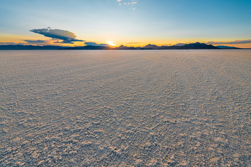 Bonneville Salt Flats low angle view with blue yellow colorful landscape sunset near Salt Lake City, Utah and silhouette view of mountains and sun setting behind clouds