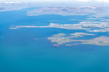 Naklejka na ściany i meble Keflavik, Iceland airport bird's eye aerial high angle view of Reykjavik city from airplane window above and colorful ocean water