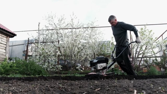 old man plowman plows the earth with a big effort motoblock. Very hard work. 4k