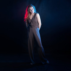 Beautiful girl model standing, studio portrait. On a black background, red and blue neon lighting. In trousers and camisole