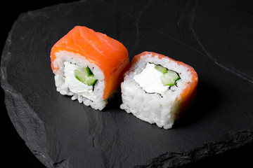 Philadelphia roll sushi with salmon on a dark background. Two pieces of philadelphia sushi roll close up on a stone Board