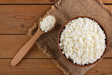 Cottage cheese on a burlap. Fresh cottage cheese in a bowl. Soft cheese and wooden spoon on a wooden boards. Top view. Copy space