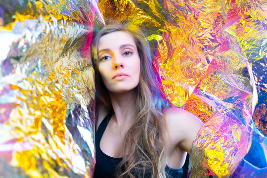 Portrait of a beautiful model girl in the studio, in shiny foil shimmering in different colors