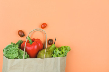 Paper bag with vegetables and fruit on an orange background.