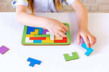 The child collects a puzzle, a constructor of colored parts, and Tetris. Large hands. The process of building the constructor. On light background