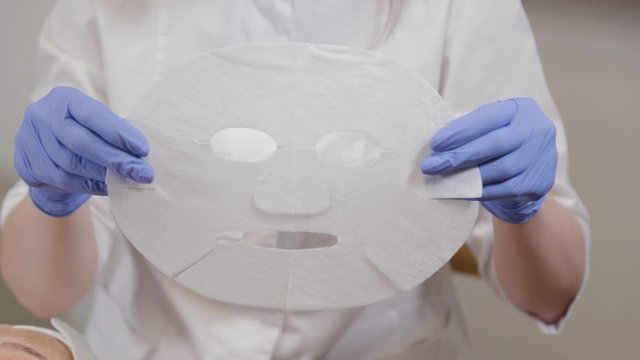 Professional unwraps paper face mask. Cosmetology.