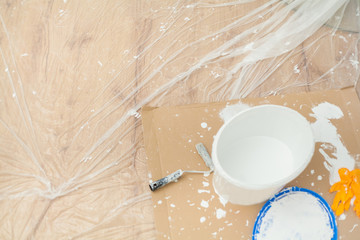 Almost empty paint bucket surrounded by paint blobs and paint residues on painter's film and cardboard Paint roller Latex gloves Handicraft training Apartment renovation Parquet floor