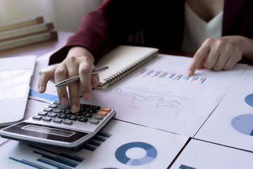 Businesswoman or Accountant hand holding pen and use calculator to calculate from analysis statistical data on table.