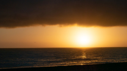 Moody sunrise shot with calm ocean, sun and thick cloud layer in upper third, shot in Kaikoura, New Zealand