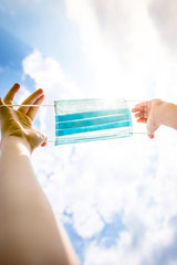 Goodbye Covid 19! Blue medical disposable face mask in the hands of a child on a background of blue...
