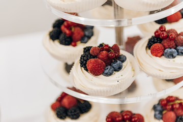 Tasty merengues covered with fresh berries lie on a cake stand, close up