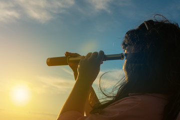 Girl looks in a monocular telescope on a sunset background. Business concept idea, look into the future, peep, see a new one. Outdoors! - obrazy, fototapety, plakaty