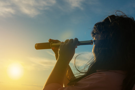 Girl looks in a monocular telescope on a sunset background. Business concept idea, look into the future, peep, see a new one. Outdoors!