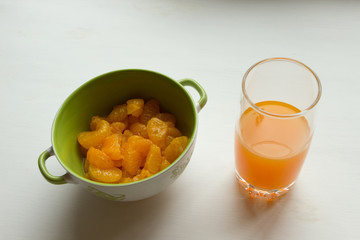 Canned tangerines in sweet sugar syrup are in a deep bowl, next to a glass of tangerine juice.