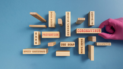Wooden blocks with written words about the concept of coronavirus and its prevention. Hand with glove and smooth blue background.