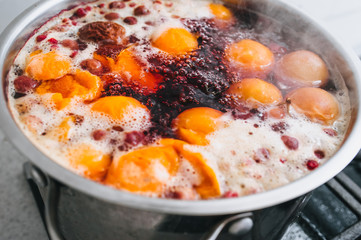 Fresh fruits: apricots, cherries, raspberries, apples are boiled in boiling water in a metal pan on a stove with bubbles and foam close-up. Cooking delicious homemade compote. Photography, concept.
