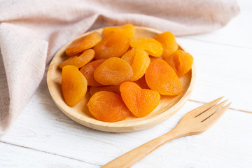 Dried apricots in wooden plate     on white wooden background with table cloth and fork, close up.