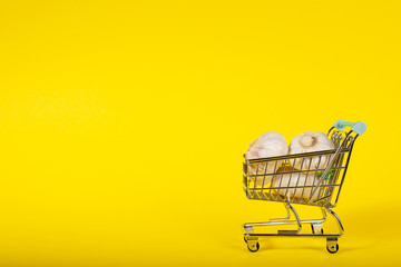 Garlic in a small toy cart on a banana yellow background. online shop delivery concept