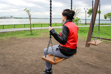 A teenage girl sitting on a swing on the lake shore.