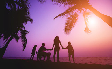 Disabled man in a wheelchair with his family on the beach. Silhouettes at sunset