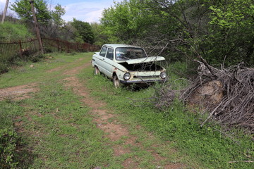 An abandoned car is parked by the road. People drove it and then abandoned it. Now the car is in the woods