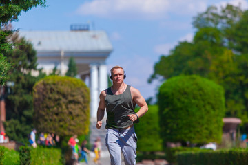 Front view of muscular young man in headphones runs in a summer Park. Running in the fresh air