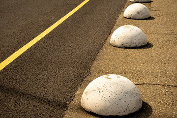 Fototapeta na wymiar Round spheric white concrete barriers on the asphalt road next to a yellow line.