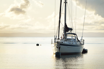 A two-masted sailboat (ketch) with a motorboat anchored on mooring near the shore of Craighouse at...