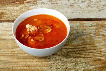 Traditional tom yam soup with chicken in a plate on a wooden table. Horizontal photo