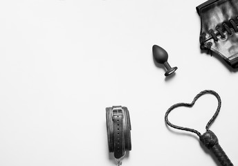 Accessories for bdsm on a white background. Leather handcuffs, butt plug, whip and corset for...