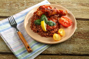 Chicken legs with red rice in tomato-garlic sauce on a plate on a wooden table