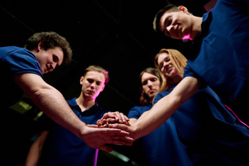 Team of five successful young e-sports clubbers making pile of hands