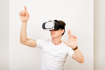 Male using virtual reality headset interacts with augmented things orienting in three dimensional space while sitting on his desk with keyboard and laptop on white background.
