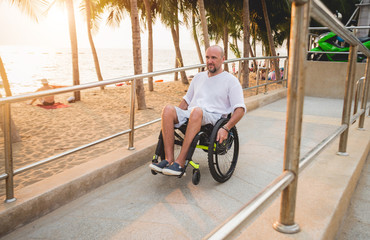 Disabled man in a wheelchair moves on a ramp to the beach.