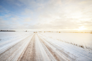 Snow-covered S shape country road through the fields after a blizzard at sunset. Old rustic house...